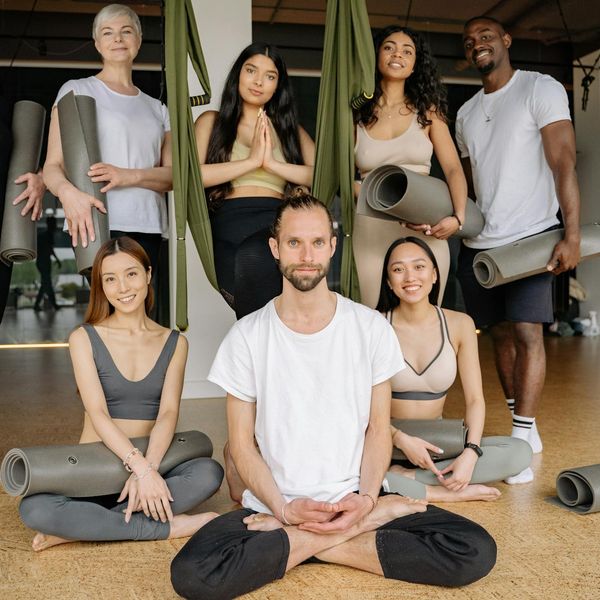 A diverse group of people smiling and stretching in a bright studio.